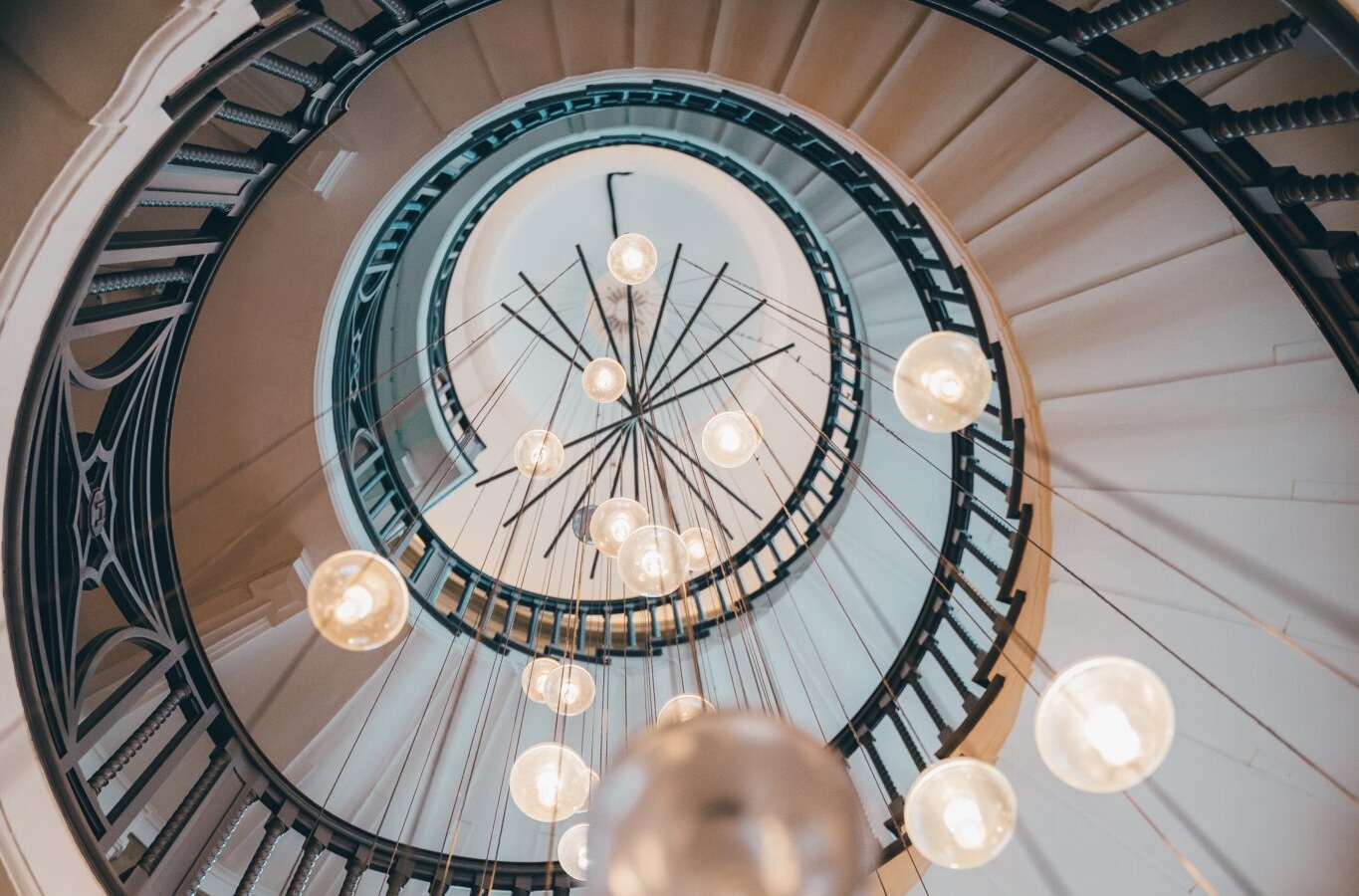 Looking up through a grand spiral staircase featuring a contemporary multi-drop chandelier with glowing glass globe pendant lights suspended through the centre atrium.