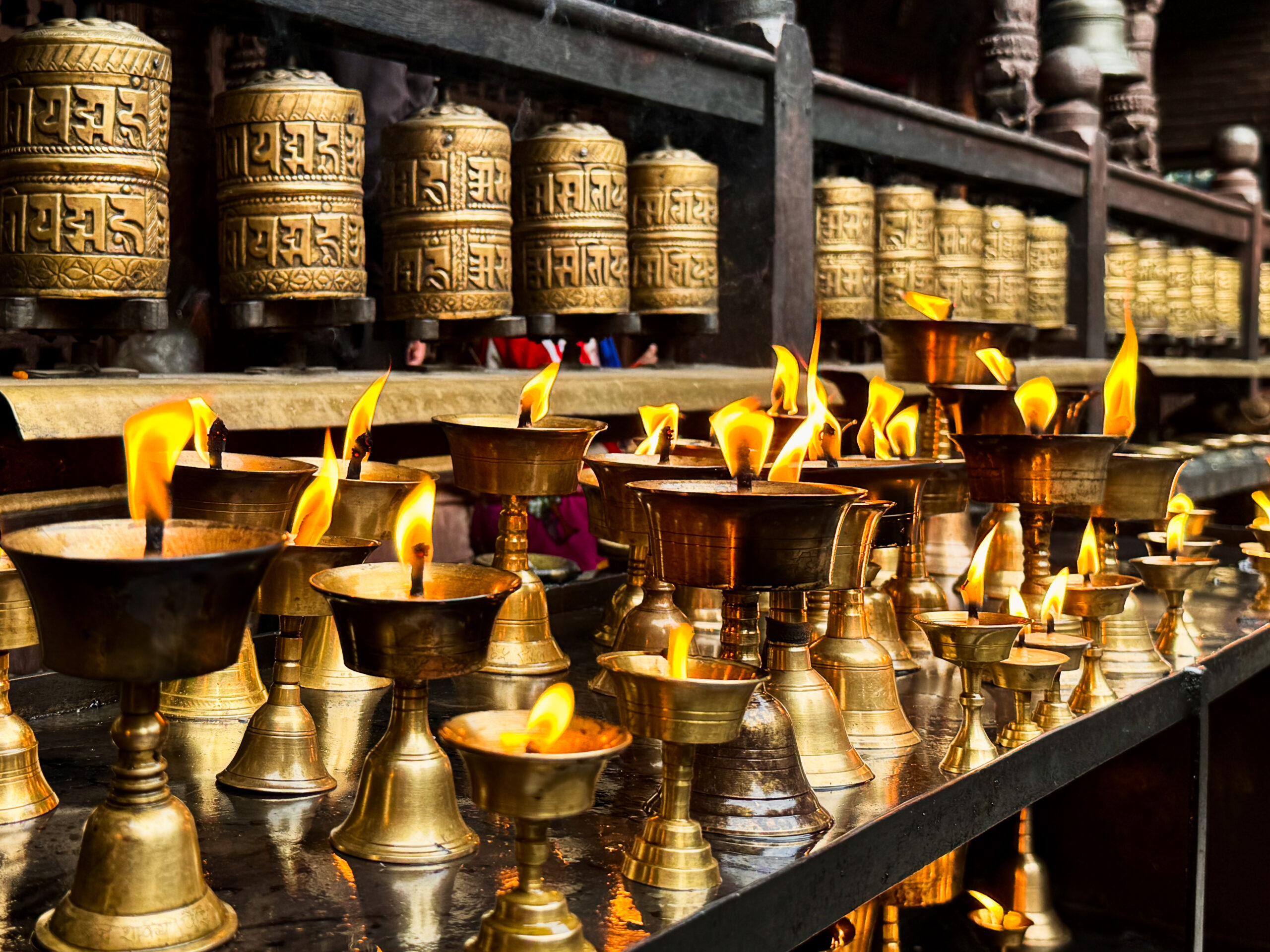 Traditional Buddhist butter lamps burning beneath rows of engraved prayer wheels inside a temple in Nepal.