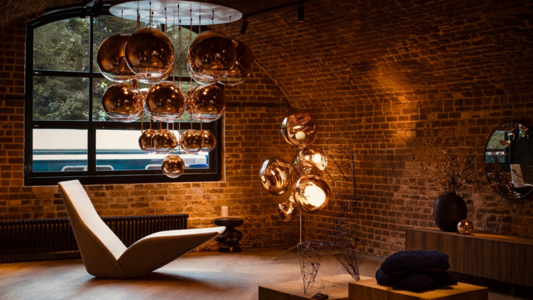 Cluster of reflective copper pendant lights in a Tom Dixon showroom with exposed brick walls and modern lounge furniture