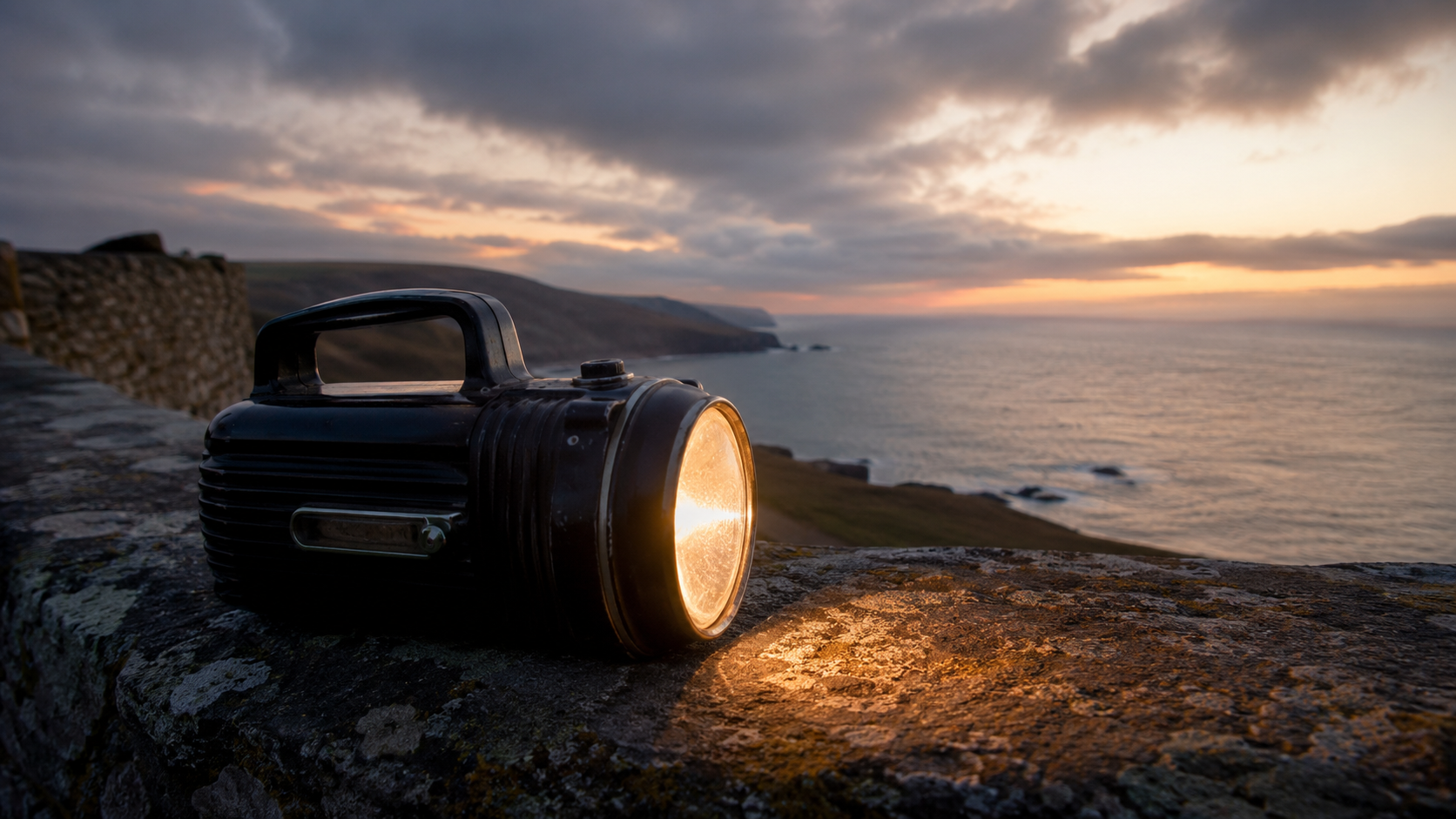 Vintage Pifco-style electric torch glowing on a stone wall overlooking a rugged coastline at sunset, illustrating the heritage of portable British lighting.