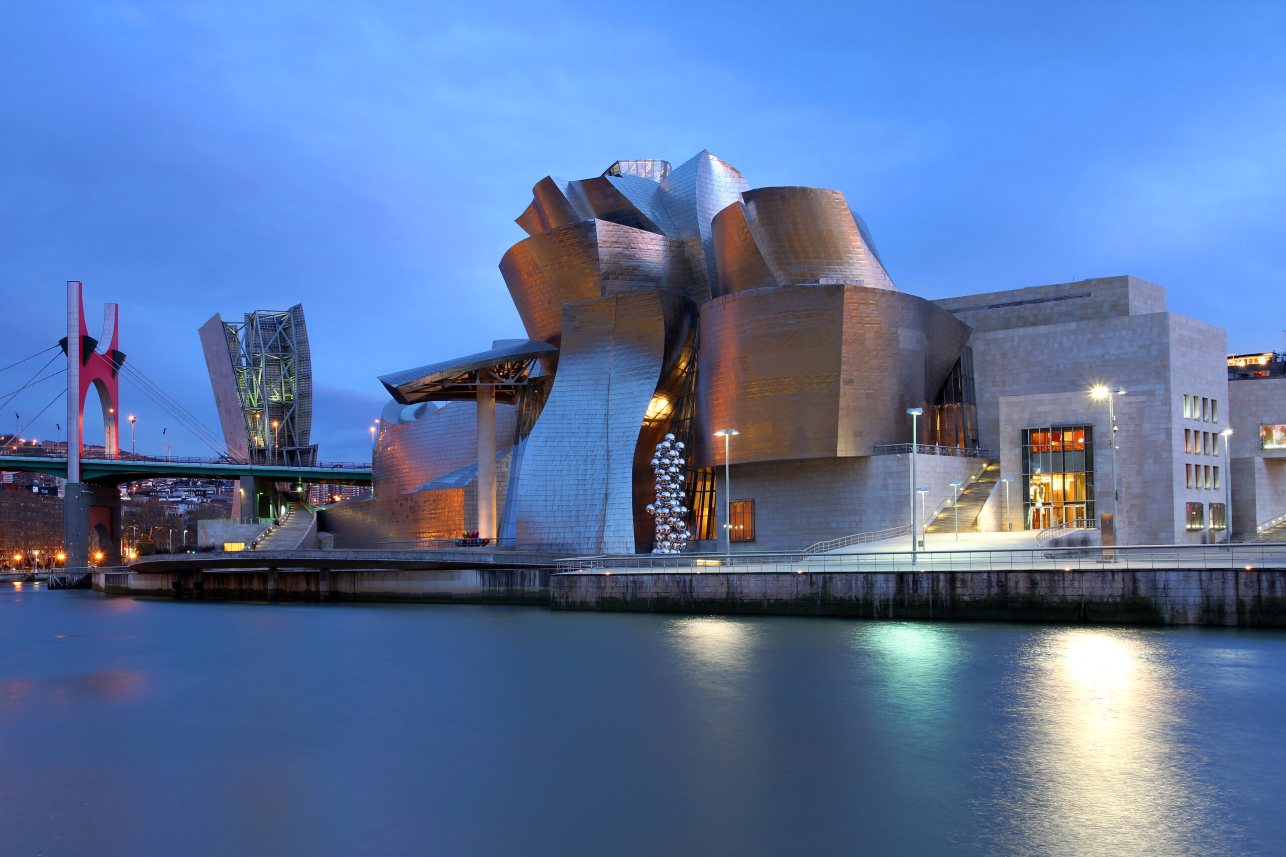 Guggenheim Museum Bilbao illuminated beside the Nervión River at dusk