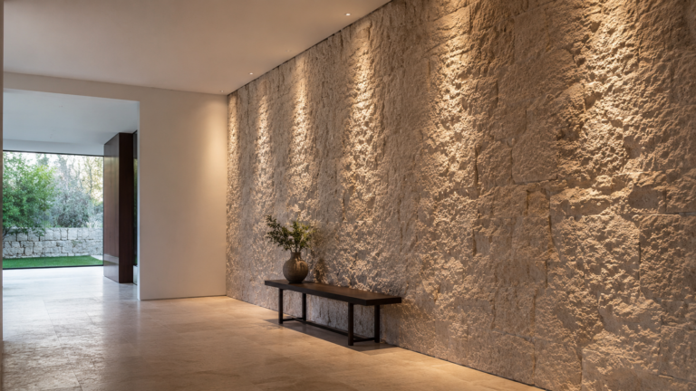 Recessed wall-grazing luminaires revealing the texture of a full-height limestone wall in a contemporary interior.