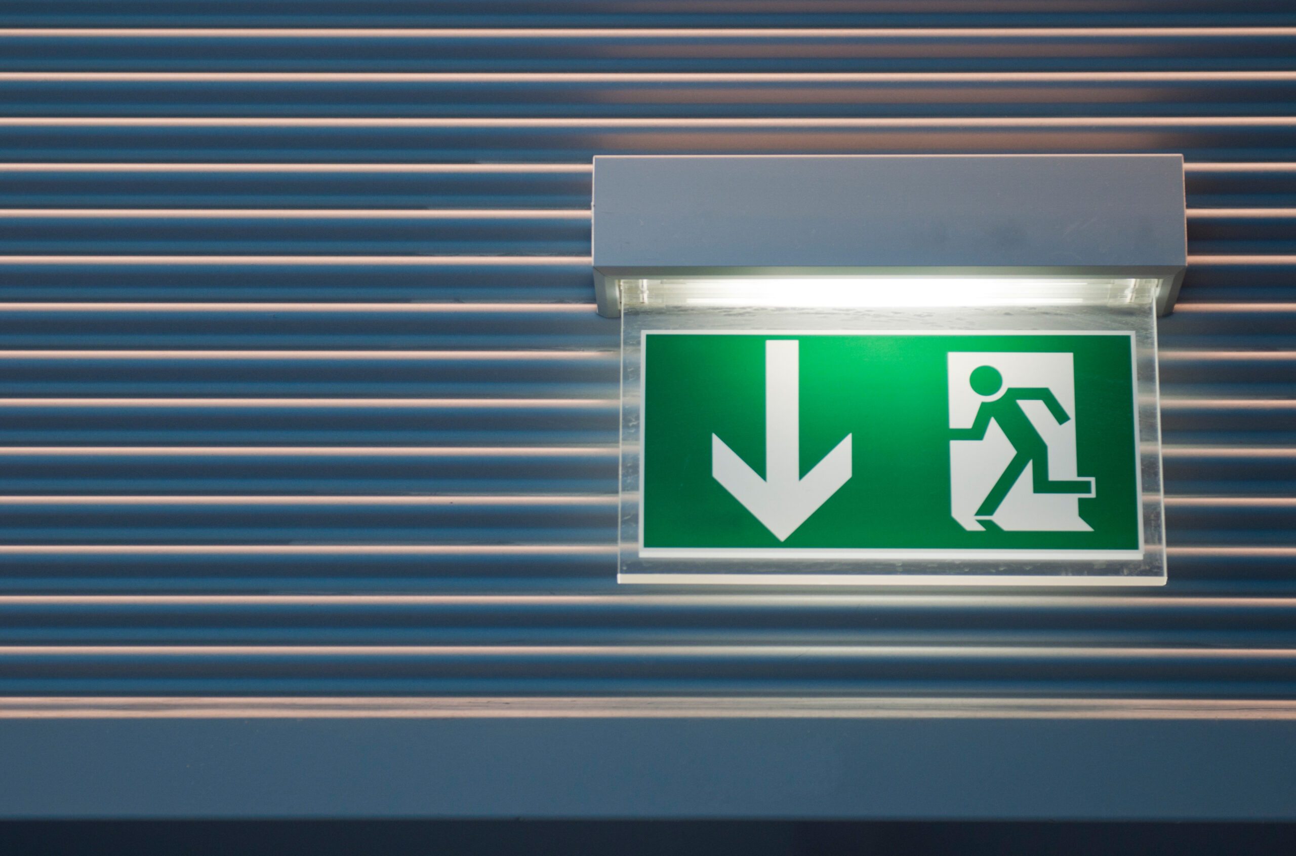 Illuminated emergency exit sign with integrated emergency lighting above an escape route.
